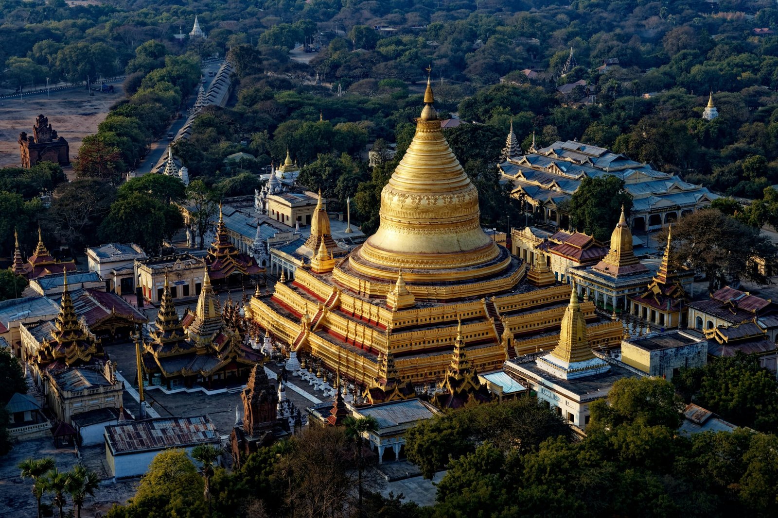 Aerial view of the Shwezigon Pagoda in Bagan, Myanmar, showcasing its golden stupa and surrounding temple complex amidst dense greenery.